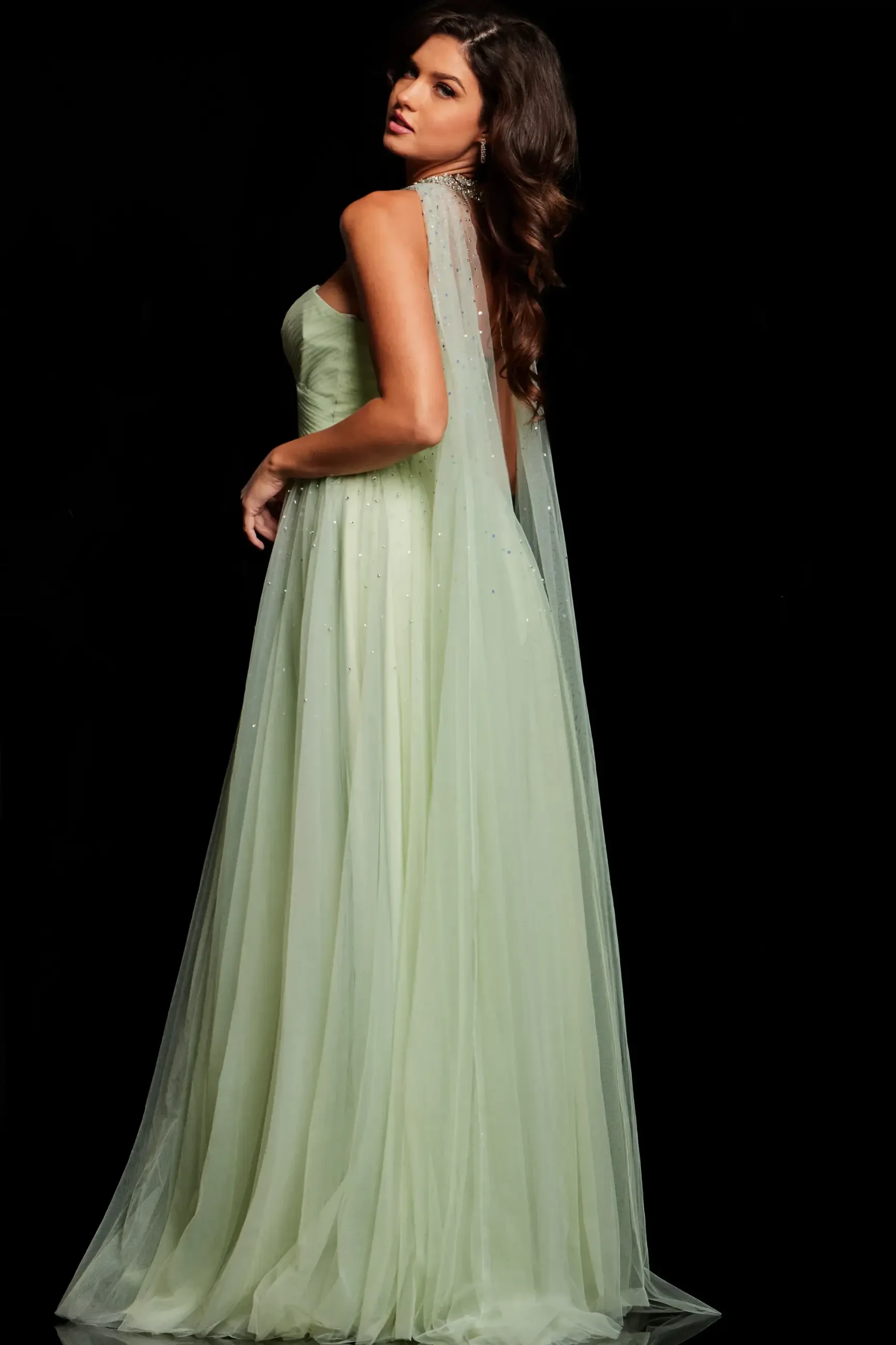 A woman wearing a light green gown with a flowing cape, standing in profile against a black background.